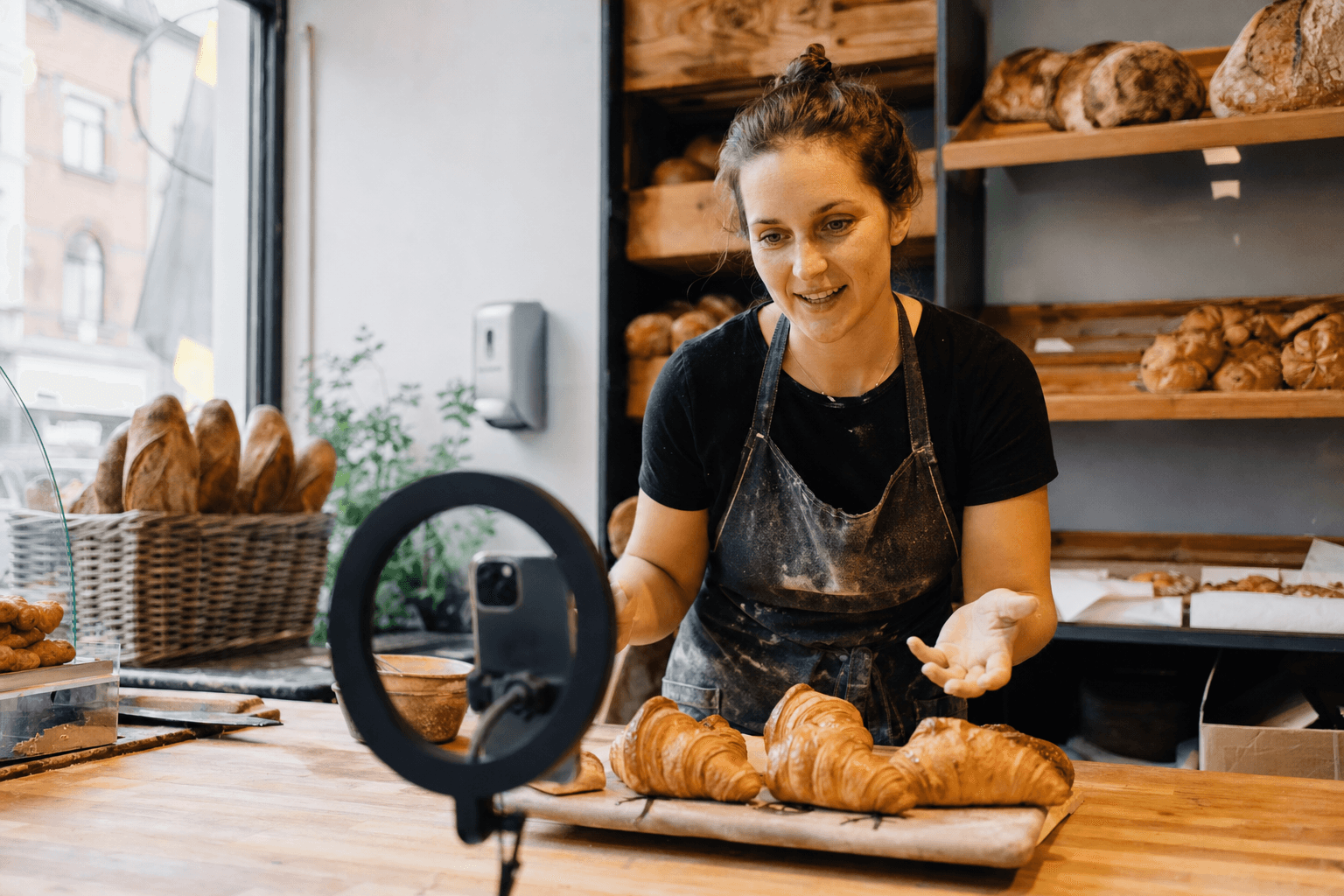 Artisan boulanger belge filmant une courte vidéo de croissants frais sur smartphone, lumière chaude de fenêtre