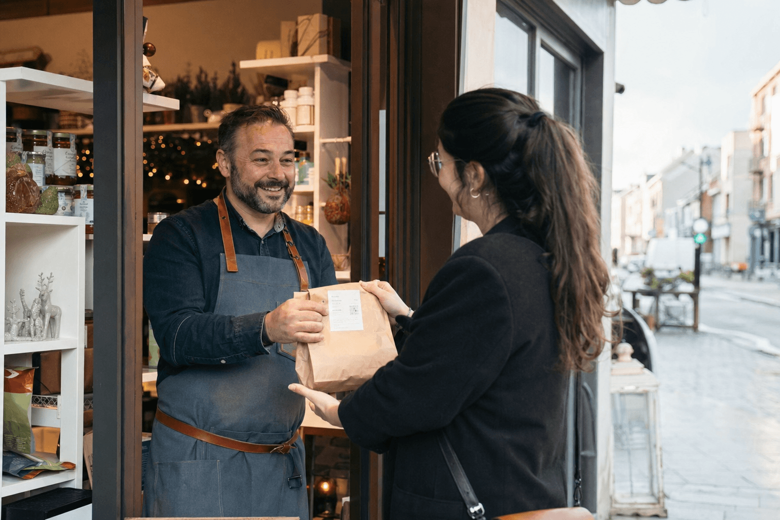 Rue commerçante animée de La Louvière, commerçant remettant un colis click & collect à un client souriant