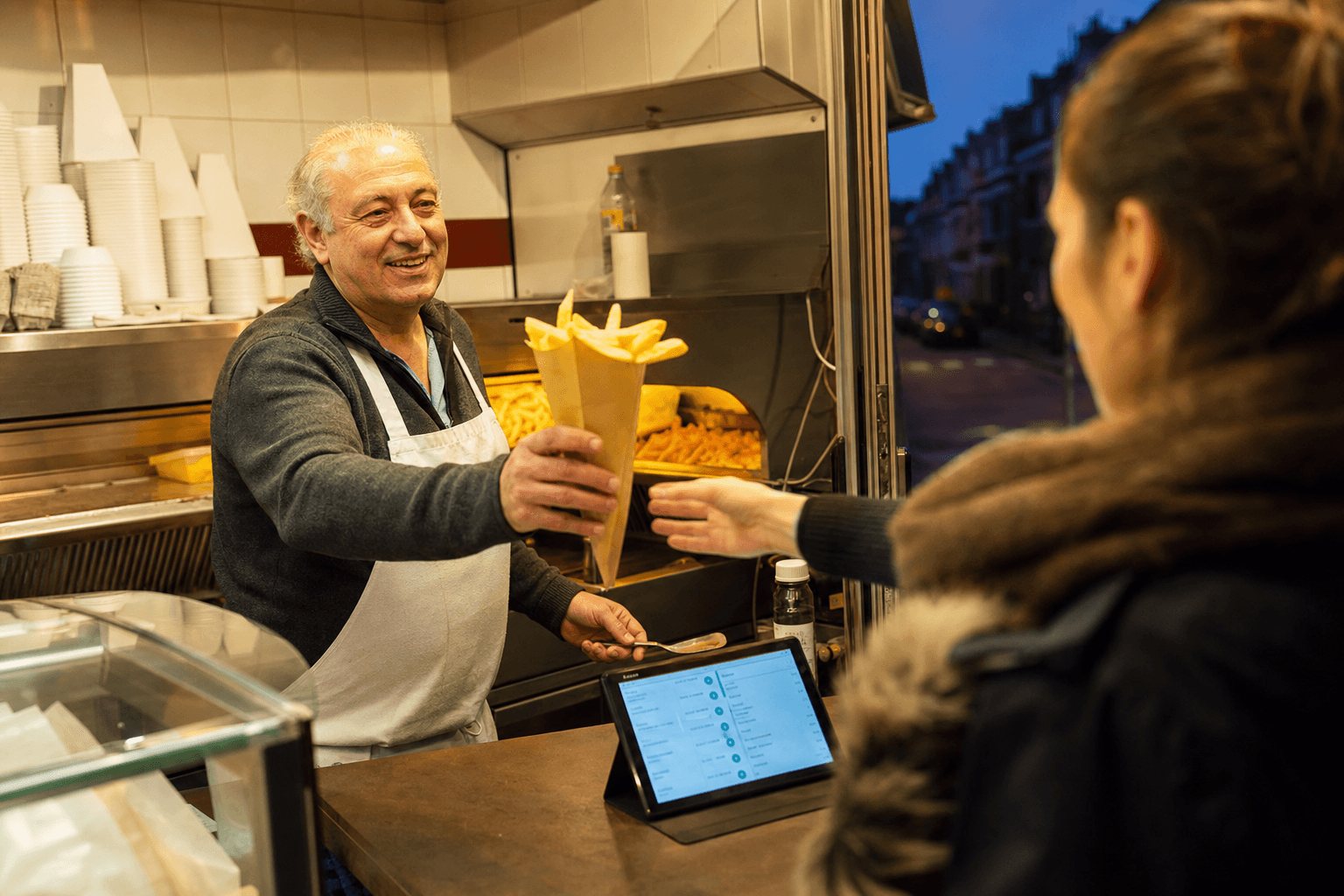 Comptoir de friterie belge avec un cornet de frites doré et un téléphone affichant une confirmation de commande click & collect